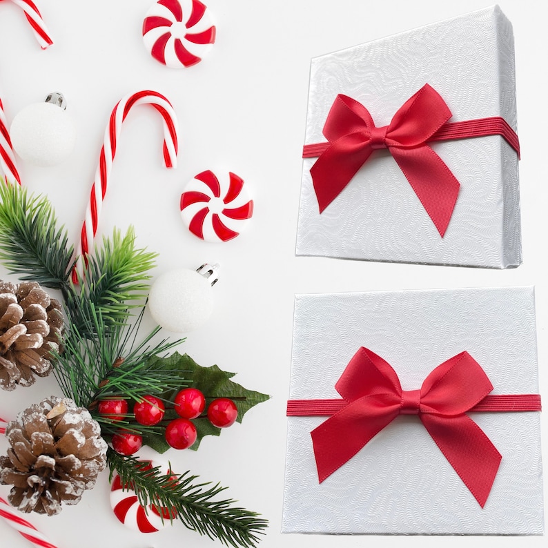 Puede incluir: Dos cajas de regalo blancas con lazos de sat&eacute;n rojo. Las cajas est&aacute;n sobre un fondo blanco con bastones de caramelo rojo y blanco, adornos y una rama de vegetaci&oacute;n.