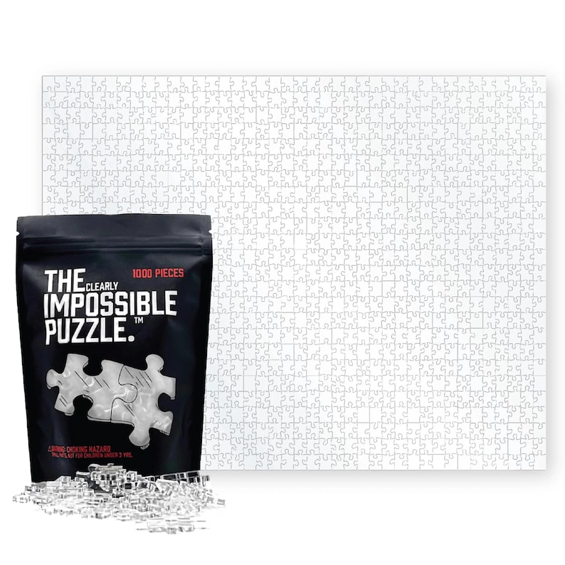 May include: A black bag with the text "The Clearly Impossible Puzzle" and a picture of a puzzle with 1000 pieces. The bag is sitting in front of a white 1000 piece puzzle.