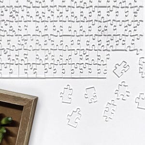 May include: A white jigsaw puzzle with several pieces missing. The pieces are scattered on a white surface. A wooden picture frame is in the lower left corner of the image.