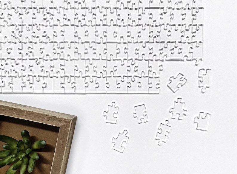 May include: A white jigsaw puzzle with several pieces missing. The pieces are scattered on a white surface. A wooden picture frame is in the lower left corner of the image.