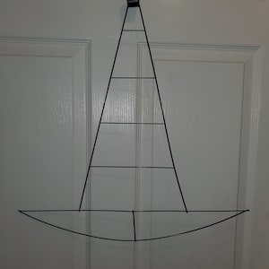 May include: A black metal wire wreath frame shaped like a witch's hat. The frame has a rounded base and a pointed top with four horizontal wires.