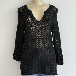 May include: Black open-knit long-sleeve top with a V-neck. The top has a loose, airy weave and a slightly flared sleeve. The garment is displayed on a mannequin and appears to be a lightweight knit.
