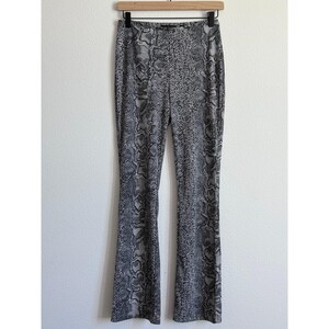 May include: A pair of high-waisted, flared pants with a snakeskin print in shades of gray and black. The pants are hanging on a wooden hanger against a white wall. The fabric appears to be a stretchy material.