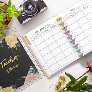 May include: A black and gold teacher planner with the text "Teacher Planner" on the cover. The planner is open to a weekly lesson plan page with the days of the week listed across the top. The planner is surrounded by a succulent plant, a camera, a rose, and gold beads.