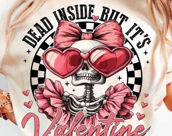 May include: A white t-shirt with a graphic design of a skeleton wearing pink heart-shaped sunglasses, a pink bow, and pink ruffles. The text "Dead Inside But It's Valentine" is written around the skeleton.