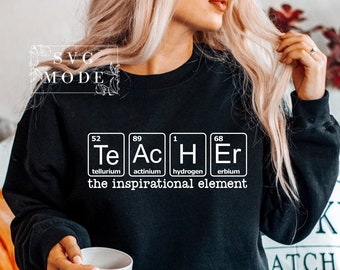 Może przedstawiać: Czarna bluza z białym nadrukiem słowa "TEACHER" napisanego za pomocą symboli pierwiastków chemicznych. Pod nadrukiem znajduje się tekst "the inspirational element".