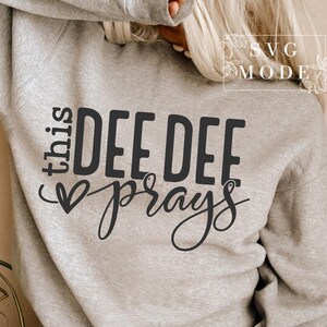 May include: A gray sweatshirt with the text "this dee dee prays" in black lettering with a heart symbol.