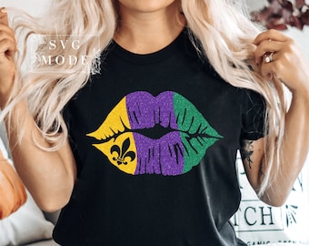 Puede incluir: Una camiseta negra con un estampado de labios de purpurina morado, verde y dorado. El estampado de labios tiene un diseño de flor de lis en el lado izquierdo.