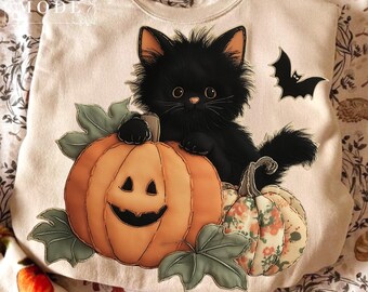 Op de afbeelding: Crèmekleurige sweatshirt met een zwarte kat op een uitgesneden pompoen. Een kleinere pompoen met bloemmotieven en een vleermuis zijn ook afgebeeld. Halloween thema.