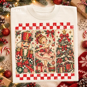 May include: A cream-coloured t-shirt featuring a vintage-style graphic with three vertical panels. The panels depict a nutcracker, a ballerina, and a Christmas tree, all framed by a red and white checkered border at the top and bottom.