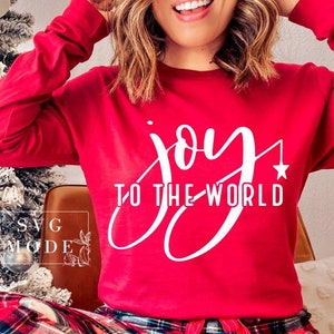 May include: Red long-sleeve shirt with white text that reads "joy to the world" in a cursive font. A small white star is above the word "world".