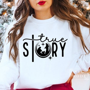 May include: White sweatshirt with black text that reads "true story" and a black silhouette of the nativity scene inside a circle.