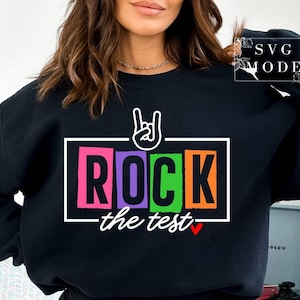 May include: Black sweatshirt with a colourful graphic that says "Rock the test" with a rock and roll hand gesture above the text.
