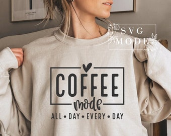 May include: Beige sweatshirt with the words "COFFEE mode ALL DAY EVERY DAY" in black. The text is inside a black rectangle with a heart above the word "COFFEE". The sweatshirt is a neutral color.