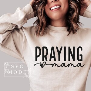 May include: A beige sweatshirt with the text "Praying mama" in black lettering with a small heart in between the words.