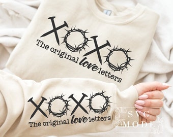 May include: Beige sweatshirt with the text "XOXO The original love letters" in black. The design includes black nail and crown of thorns graphics. The sweatshirt is displayed on a white surface.