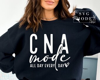 May include: Black sweatshirt with the text "CNA mode ALL DAY EVERY DAY" in white. The sweatshirt has a crew neck and long sleeves. The text is in a bold, sans-serif font with the word "mode" in a cursive font. The design includes a small heart.
