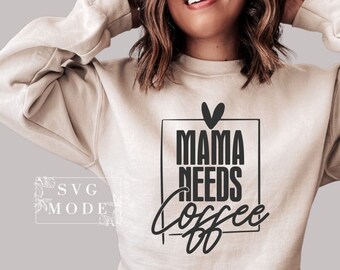 Pode incluir: Uma camisa de moletom bege com o texto "Mama Needs Coffee" em letras pretas dentro de um quadrado preto. Um coração preto está acima do texto.