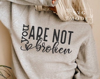 May include: A gray sweatshirt with the text "You are not broken" in black lettering with a small heart symbol.