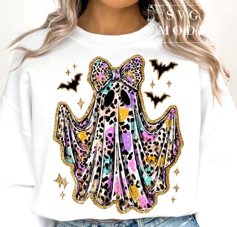 May include: White sweatshirt featuring a colorful ghost design with a bow, leopard print, and gold glitter accents. The ghost has black eyes and is surrounded by black bats and gold stars. A fun Halloween-themed design.
