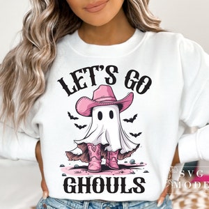 Może przedstawiać: Biała bluza z nadrukiem r&oacute;żowego ducha w r&oacute;żowym kowbojskim kapeluszu i butach. Na bluzce widnieje napis "Let's go ghouls".