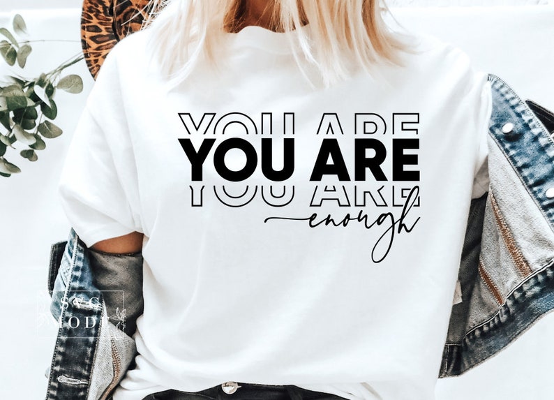 May include: White t-shirt with the text "You are You are You are enough" in black lettering.