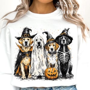 May include: White sweatshirt featuring a Halloween-themed graphic. The graphic depicts four dogs dressed in costumes: a witch, a ghost, a witch, and a skeleton, with a carved pumpkin. The dogs are in shades of black, white, and gold.