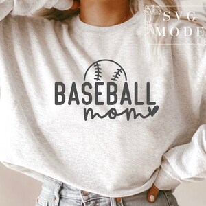 May include: A light grey sweatshirt featuring the words "BASEBALL mom" in black, with a baseball graphic above the word "mom". The sweatshirt has a crew neck.