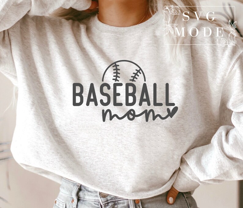May include: A light grey sweatshirt featuring the words "BASEBALL mom" in black, with a baseball graphic above the word "mom". The sweatshirt has a crew neck.