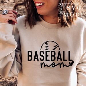 May include: A beige sweatshirt featuring the text "BASEBALL mom" in black, with a baseball graphic above "baseball". The sweatshirt is a neutral colour and has a crew neck.