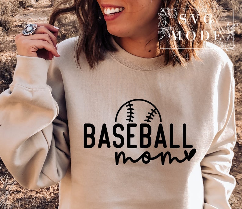 May include: A beige sweatshirt featuring the text "BASEBALL mom" in black, with a baseball graphic above "baseball". The sweatshirt is a neutral colour and has a crew neck.