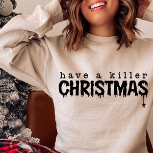 May include: A beige sweatshirt with the phrase "have a killer CHRISTMAS" printed in black. The word "CHRISTMAS" has a dripping effect, and a black star hangs from the bottom of the word. The sweatshirt is a casual holiday garment.