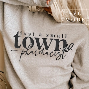 以下が含まれることがあります： グレーのトレーナーに、黒い文字で「just a small town pharmacist」と書いてあり、小さなハートのグラフィックが描かれています。