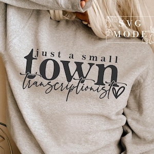 May include: A light gray sweatshirt with the text "just a small town transcriptionist" in black script and a heart symbol. The sweatshirt is a casual style.