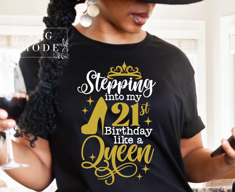 Pode incluir: Camiseta preta com um gr&aacute;fico dourado e branco. O gr&aacute;fico diz "Stepping into my 21st Birthday like a Queen" com um design de salto alto e coroa. A camisa tem gola redonda e mangas curtas.