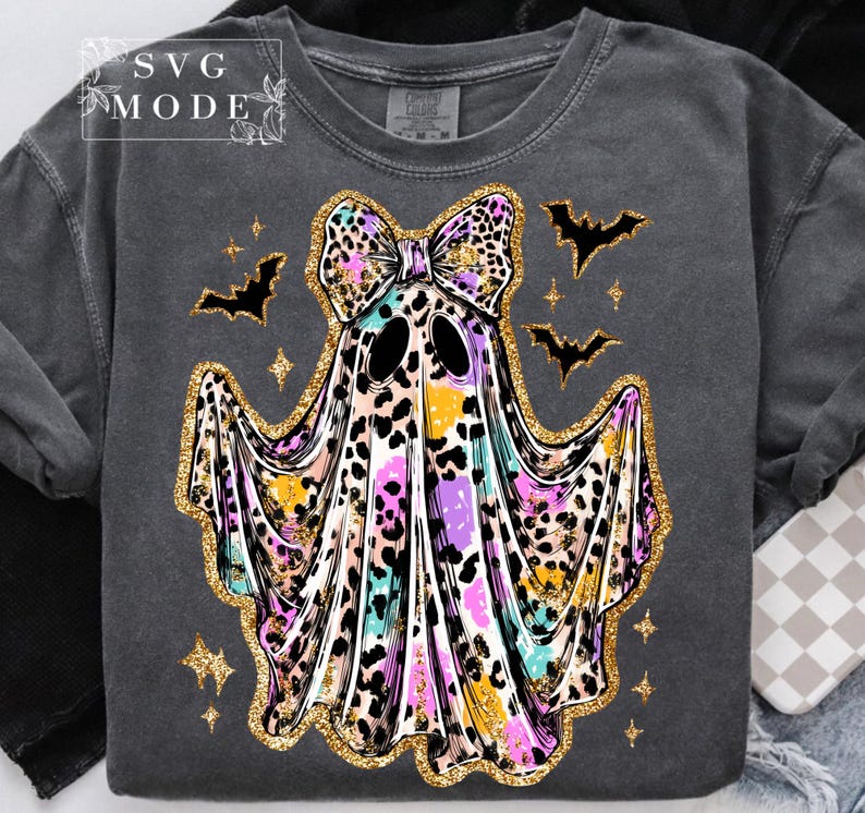 May include: Dark gray sweatshirt featuring a colorful ghost design with a leopard print bow and trim. The ghost has black eyes and is surrounded by bats and stars. The text "SVG MODE" is in the upper left corner.