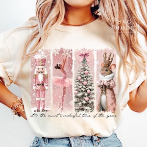 K&ouml;nnte beinhalten: Ein wei&szlig;es T-Shirt mit einem rosafarbenen Weihnachtsmotiv, das eine Ballerina, einen Nussknacker, eine Maus mit Krone und einen Weihnachtsbaum zeigt. Der Text "it's the most wonderful time of the year" ist unter dem Motiv gedruckt.