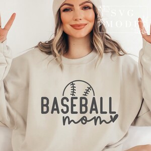 May include: A beige sweatshirt with the words "BASEBALL mom" in black, accompanied by a baseball graphic. The sweatshirt is a neutral colour and has a crew neck.