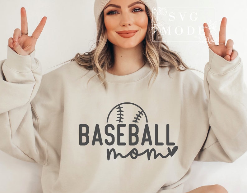 May include: A beige sweatshirt with the words "BASEBALL mom" in black, accompanied by a baseball graphic. The sweatshirt is a neutral colour and has a crew neck.