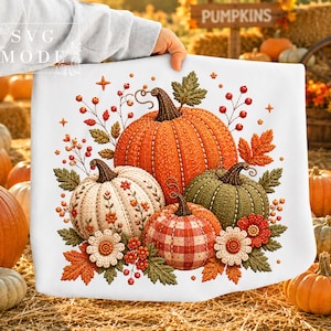 May include: A white square cushion with a fall-themed design. The design features an orange pumpkin, a green pumpkin, a white pumpkin, and a red and white plaid pumpkin, surrounded by autumn leaves and flowers.