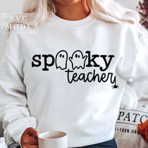 May include: White sweatshirt with black text that reads "spooky teacher" with three ghost silhouettes and a spider graphic.