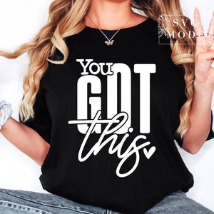May include: Black t-shirt with the white text "You Got This." The words "You" and "Got" are in a bold, blocky font, while "this" is in a cursive script. The shirt is a classic crew neck style.