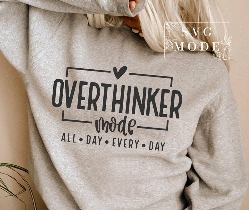 May include: A light gray sweatshirt with the words "OVERTHINKER mode ALL &bull; DAY &bull; EVERY &bull; DAY" in black lettering. The design includes a heart above the word "OVERTHINKER". The sweatshirt is a casual style.