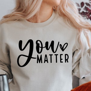 May include: A light gray sweatshirt with the text "you matter" in black cursive lettering with a small heart symbol next to the word "you".