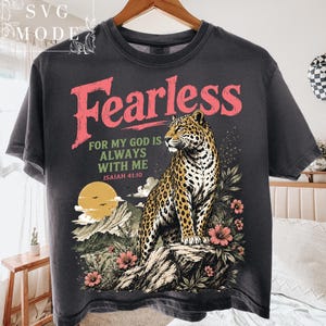 May include: Charcoal grey t-shirt with a leopard illustration, mountains, and flowers. The text "Fearless" is above the phrase "For my God is always with me" and the Bible verse Isaiah 41:10.