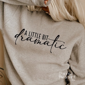 May include: A grey sweatshirt with the text "A little bit dramatic" printed in black on the front.