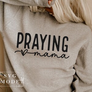 May include: A gray sweatshirt with the text "Praying mama" in black lettering with a small heart symbol.