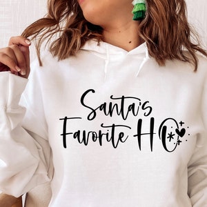 May include: White hooded sweatshirt with the text "Santa's Favourite Ho" in black cursive lettering. A small black heart with a snowflake and stars is next to the text.