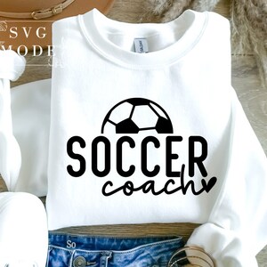 May include: White sweatshirt with a black football graphic and the text "SOCCER coach" with a heart.