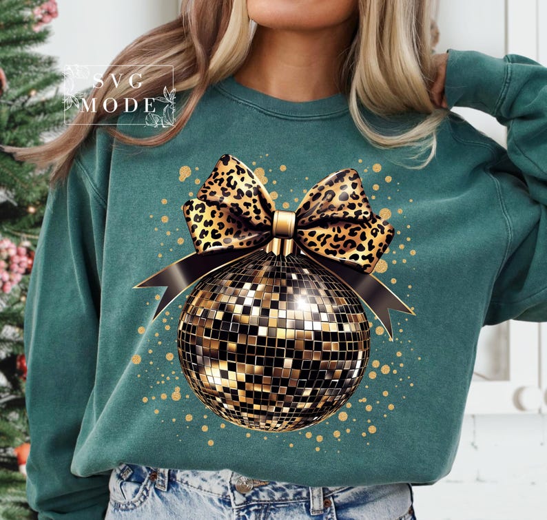 May include: A teal sweatshirt with a gold and black disco ball ornament with a leopard print bow. The ornament is surrounded by gold glitter.